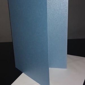 Peut inclure: Une carte bleu clair avec une finition l&eacute;g&egrave;rement scintillante, pli&eacute;e en deux et plac&eacute;e sur une enveloppe blanche.