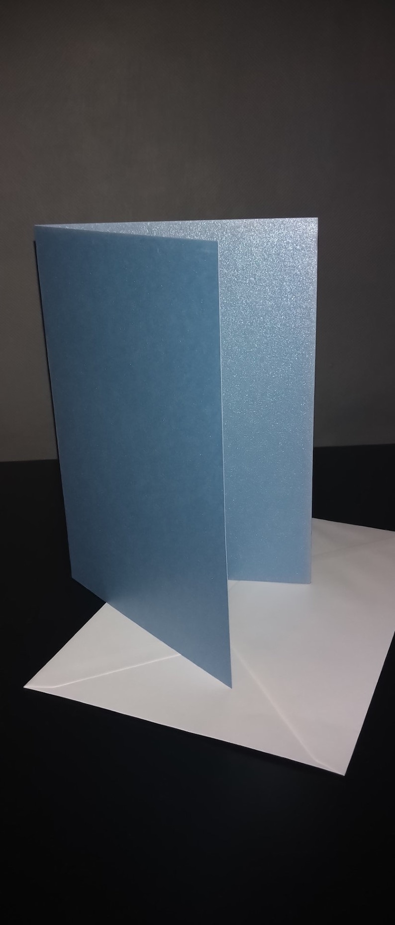 Peut inclure: Une carte bleu clair avec une finition l&eacute;g&egrave;rement scintillante, pli&eacute;e en deux et plac&eacute;e sur une enveloppe blanche.
