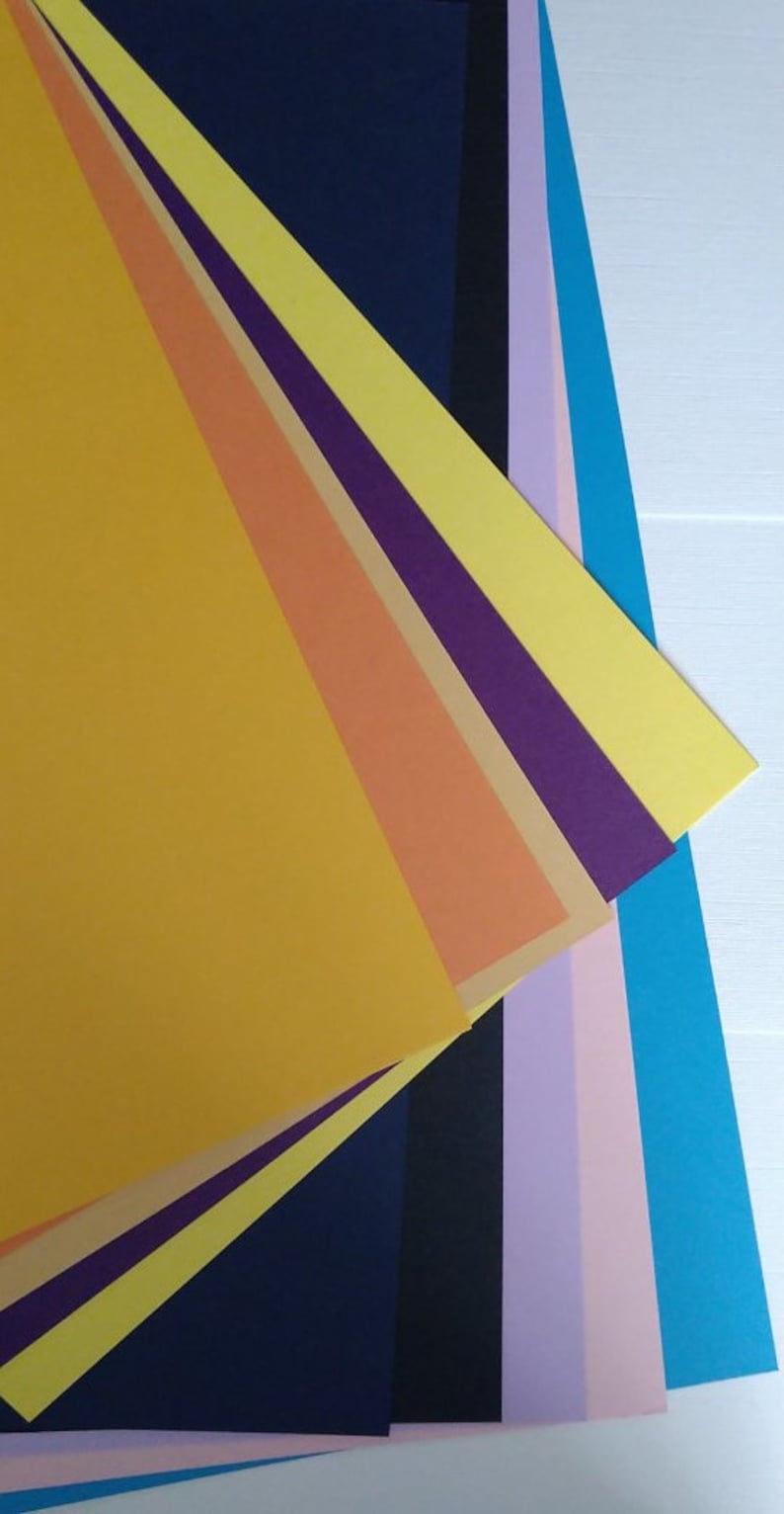 May include: A stack of colorful paper sheets in various shades of yellow, orange, purple, blue, and pink. The sheets are arranged in a fan shape, with the yellow sheet at the top and the pink sheet at the bottom.