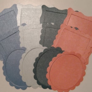 May include: A selection of paper cutouts in various shapes and colours. The shapes include squares, circles, and frames with scalloped edges. Colours include blue, white, grey, and coral.