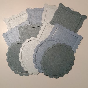 May include: A collection of decorative paper frames and circles in various shades of grey and silver. The frames and circles have scalloped edges and are perfect for adding a touch of elegance to crafts and scrapbooking projects.