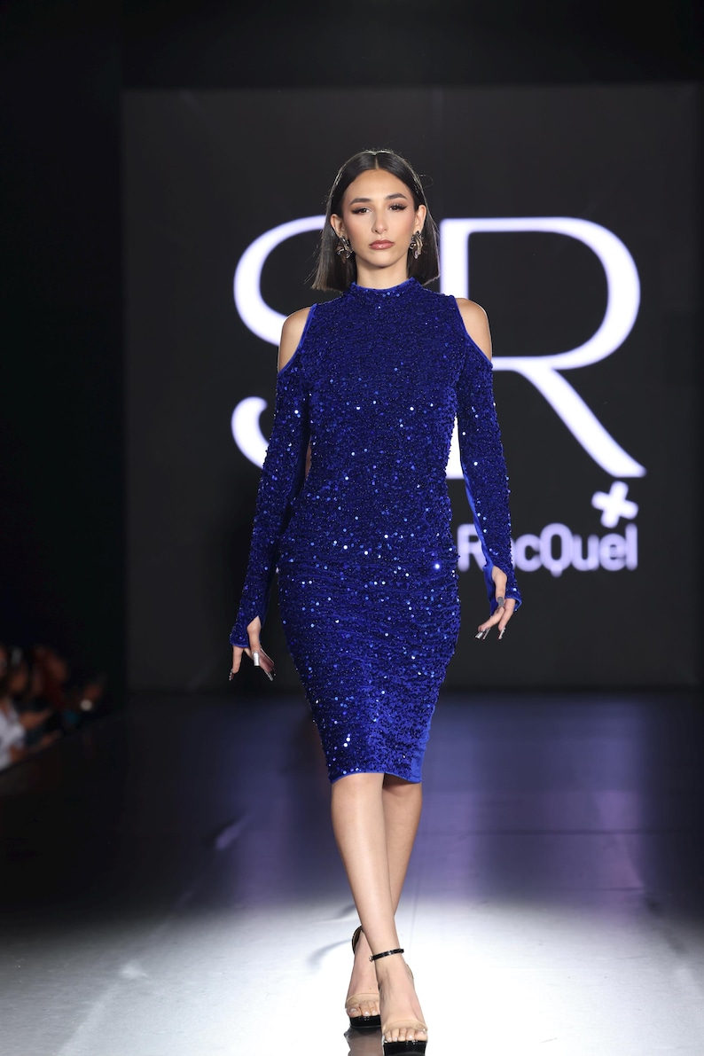 May include: A woman in a royal blue, sequined, long-sleeved dress with shoulder cutouts. The dress is knee-length and has a high neckline. She is wearing black heels. The background is dark with white text.