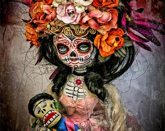 May include: A Day of the Dead doll with a skull face and floral crown holds a smaller doll with a skull face. The larger doll is wearing a pink dress with lace trim. The background is a dark, textured surface.