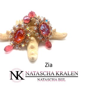 May include: A pair of red and gold beaded earrings with a large, oval-shaped, iridescent red gemstone in the centre of each earring. The earrings are hanging from a starfish-shaped stand.