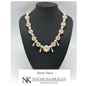May include: A delicate gold and white beaded necklace with a large, sparkling crystal pendant. The necklace is displayed on a black mannequin bust. The text "Anne Fleur" and "NATASCHA KRALEN" is visible below the necklace.