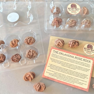 May include: Oklahoma Rose Rocks in clear plastic containers, with a Red Dirt Roses sticker. The rocks are a reddish-brown colour and have a unique, rose-like shape. A card with text about the rocks is also visible.