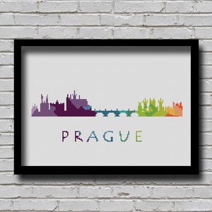 May include: A framed cross-stitch design of the Prague skyline in a rainbow of colors. The skyline includes buildings and a bridge. The word "PRAGUE" is stitched in black below the skyline.