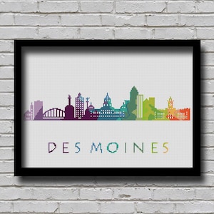 Könnte beinhalten: Ein farbenfrohes Kreuzstich-Design der Skyline von Des Moines. Die Gebäude sind in verschiedenen Schattierungen von Lila, Blau, Grün, Gelb, Orange und Rot umrandet. Der Text "DES MOINES" ist in Weiß unterhalb der Skyline gestickt.