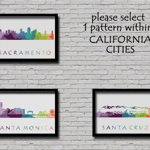 May include: Three framed prints of city skylines with colorful outlines. The prints are on a white brick wall. The text on the prints reads "Sacramento", "Santa Monica", and "Santa Cruz".