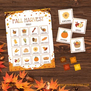 May include: A printable Fall Harvest Bingo game with a white background and orange and brown accents. The bingo card features images of fall harvest items such as pumpkins, apples, corn, and leaves. There are also separate cards with images of each item to use as markers.