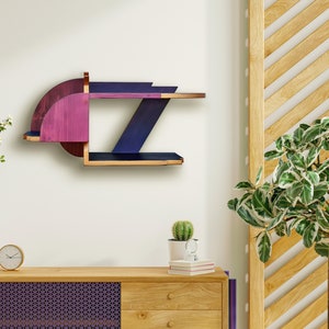 Op de afbeelding: Een geometrisch houten plank met twee planken, geschilderd in tinten paars en blauw. De plank is gemonteerd aan een witte muur.