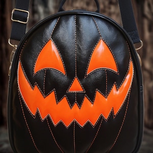 May include: Black pumpkin-shaped backpack with orange accents. The bag features a jack-o'-lantern face design with stitched details. Includes a top handle and adjustable shoulder straps. A fun accessory for Halloween.