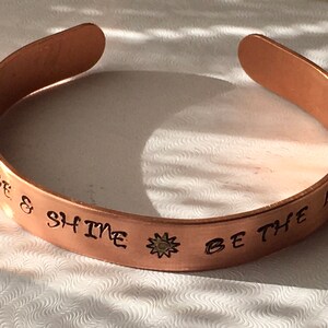May include: Copper bracelet with the words "Rise & Shine Be The Light" engraved on it. A small sun design is centered on the bracelet.