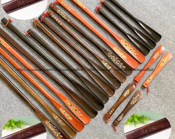 Pode incluir: Uma coleção de calçadores de madeira com designs intrincados e detalhes dourados. Alguns dos calçadores são pintados de vermelho e preto, enquanto outros são de madeira natural. Os calçadores estão dispostos em uma fila sobre uma superfície branca. O texto "SGS" está gravado em alguns dos calçadores.