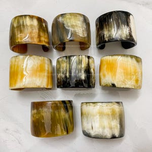 May include: Eight horn bracelets in various shades of brown, yellow, and black. The bracelets are made of natural horn and have a polished finish.