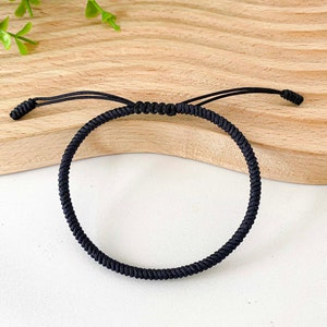 Könnte beinhalten: Ein schwarzes geflochtenes Armband mit einem geknoteten Verschluss.