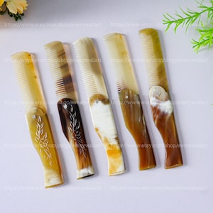 May include: Five brown and white horn combs with intricate floral designs. The combs are all the same size and shape, and they are arranged in a row on a white surface.