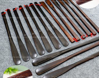 Pode incluir: Um conjunto de 18 calçadores de madeira, alguns com acabamento marrom escuro e outros com acabamento de madeira natural. Os calçadores estão dispostos em filas sobre uma superfície cinza. Os calçadores medem todos aproximadamente 30 cm de comprimento. Os calçadores têm uma ponta arredondada e uma alça plana. Os calçadores são uma ferramenta útil para calçar sapatos.