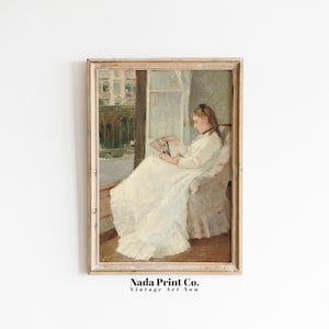May include: A vintage painting of a woman in a white dress sitting in a chair and reading a book. The painting is framed in a light wood frame.
