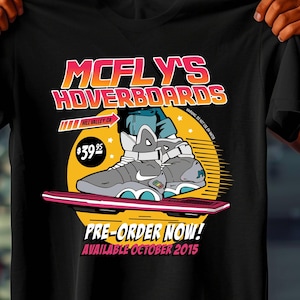 May include: Black t-shirt with a graphic of a hoverboard and the text "McFly's Hoverboards". The design includes a futuristic sneaker and the words "Pre-Order Now! Available October 2015".