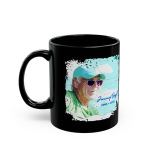 Pode incluir: Caneca de cerâmica preta com um retrato de Jimmy Buffett usando óculos de sol e boné. O retrato está em um fundo azul claro com o texto "Jimmy Buffett 1946-2023". A caneca tem uma alça curva.