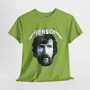 May include: A green t-shirt with a black and white image of Jim Henson, the creator of the Muppets. The text "HENSON" is above the image and "MASTER OF PUPPETS" is below the image.
