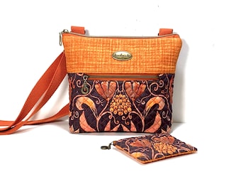 May include: A quilted crossbody bag with an orange top panel and a dark purple lower section featuring an orange floral pattern. The bag has an orange strap, a zipper closure, and a metal tag labeled handmade. A matching small square pouch is included.