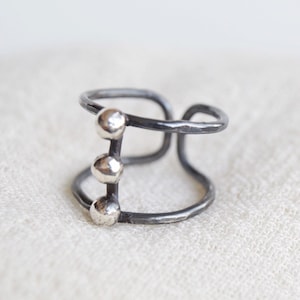 Peut inclure: Une bague en argent avec trois petites boules argentées sur une bande noire.