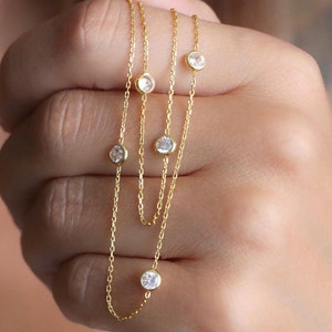Close-up of a hand showcasing a diamond station necklace, featuring sparkling CZ diamonds in natural light for maximum brilliance.