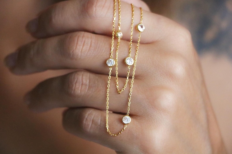 Hand holding a diamond station necklace with sparkling CZ diamonds, close-up shot highlighting the brilliance and shine of the stones.
