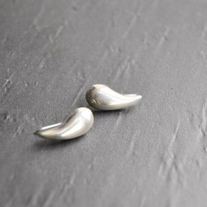 May include: A pair of silver teardrop-shaped earrings. The earrings are smooth and have a polished finish.