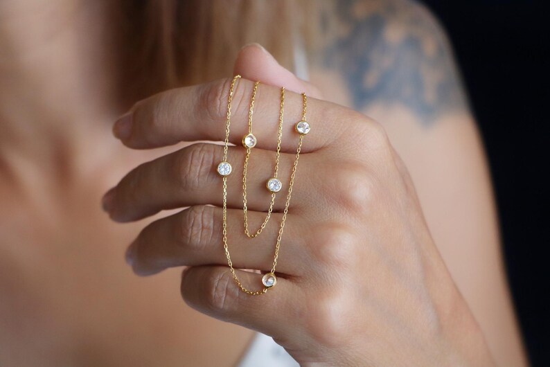Hand holding a CZ diamond station necklace, focusing on the shimmering stones and elegant design in a close-up view.