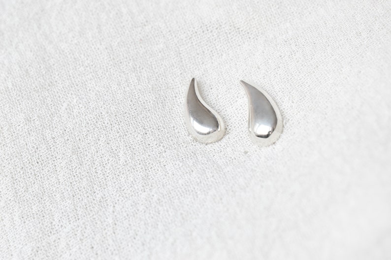 May include: A pair of silver teardrop-shaped earrings.