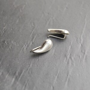 May include: A pair of silver teardrop-shaped earrings with a curved hook closure.