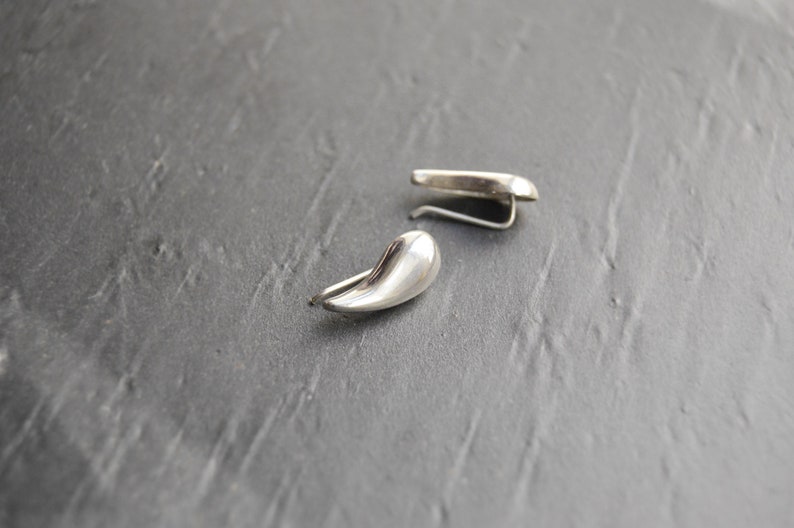 May include: A pair of silver teardrop-shaped earrings with a curved hook closure.