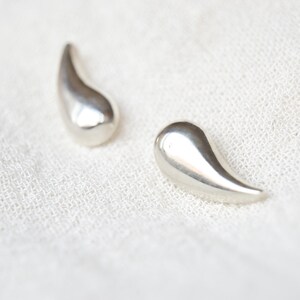 May include: A pair of silver teardrop-shaped earrings. The earrings are smooth and shiny.