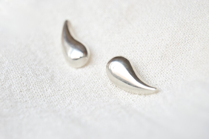 May include: A pair of silver teardrop-shaped earrings. The earrings are smooth and shiny.