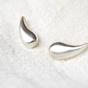 May include: A pair of silver teardrop-shaped earrings. The earrings are smooth and shiny.