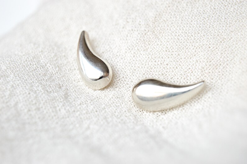 May include: A pair of silver teardrop-shaped earrings. The earrings are smooth and shiny.