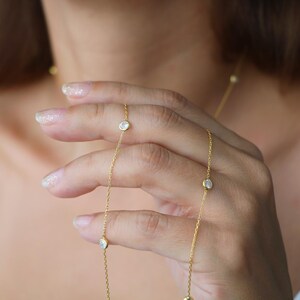 Detail shot of a diamond station necklace held by hand, emphasizing the clarity and shine of the CZ diamonds against a soft background.