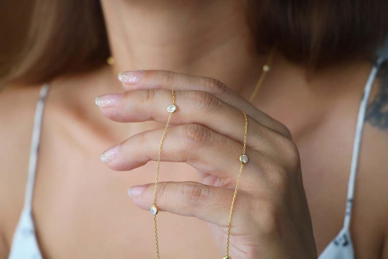 Detail shot of a diamond station necklace held by hand, emphasizing the clarity and shine of the CZ diamonds against a soft background.