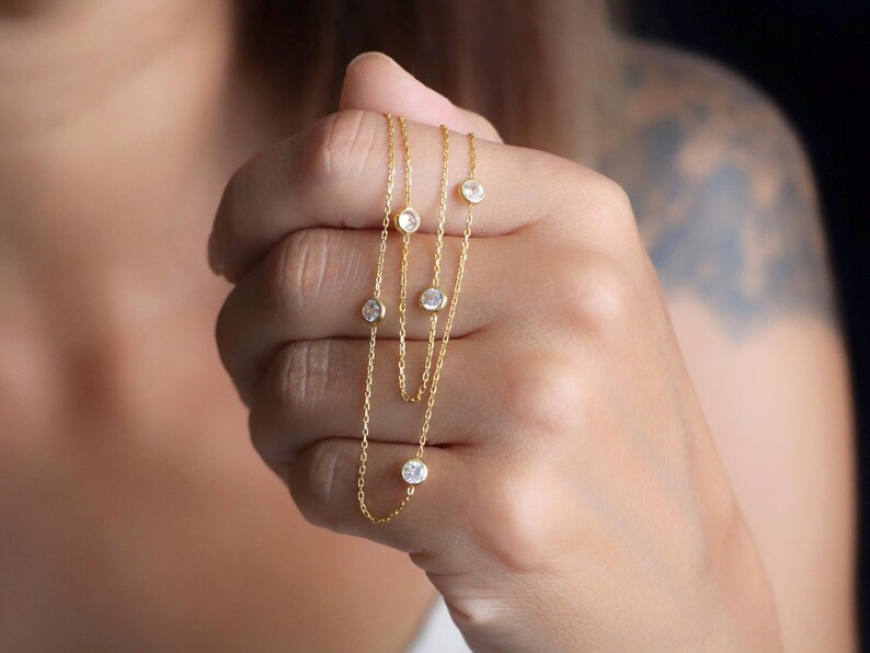 Close-up of a hand showcasing a diamond station necklace, featuring sparkling CZ diamonds in natural light for maximum brilliance.