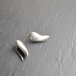 May include: A pair of silver teardrop shaped earrings. The earrings are smooth and have a slightly curved shape.