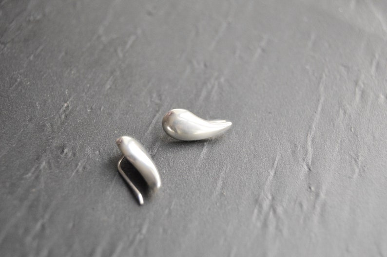 May include: A pair of silver teardrop shaped earrings. The earrings are smooth and have a slightly curved shape.