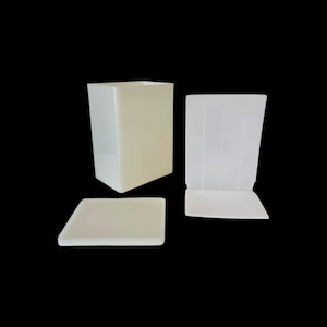 Puede incluir: Juego de tres recipientes de acrílico translúcido blanco roto. Incluye una caja cuadrada, una bandeja rectangular y un soporte con frente curvo. Los objetos están dispuestos sobre un fondo negro.