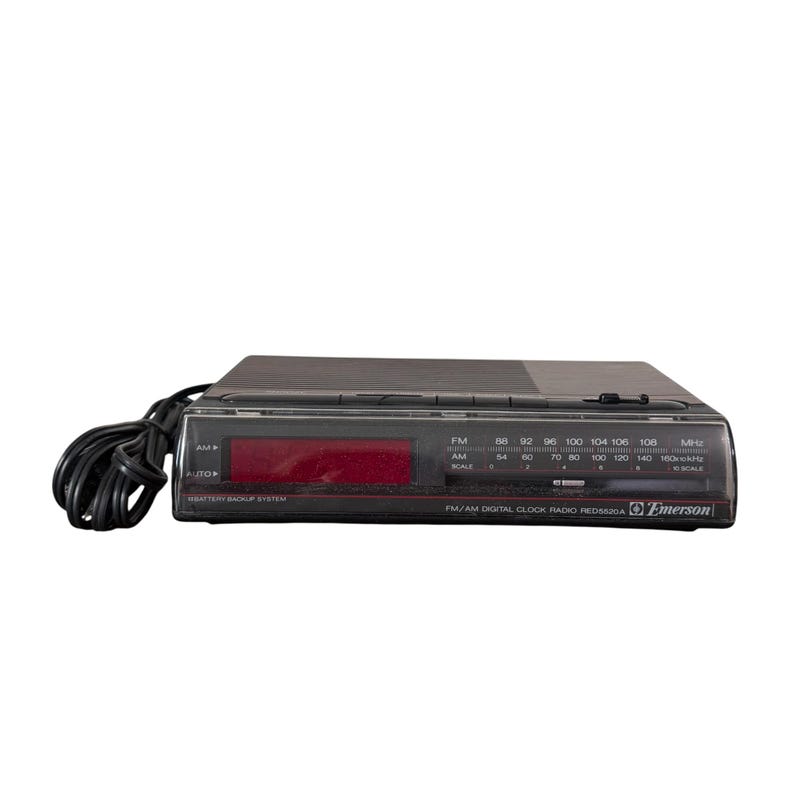 Puede incluir: Un radio reloj digital FM/AM Emerson negro con una pantalla digital roja. La radio tiene un cable de alimentaci&oacute;n negro y botones para estaciones de radio AM/FM. La radio tiene un sistema de respaldo de bater&iacute;a.