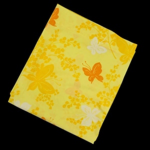 May include: A folded yellow fabric with a repeating pattern of orange and white butterflies and floral elements. The butterflies have detailed wing patterns, and the floral elements are in shades of yellow and orange.