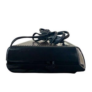 Puede incluir: Un despertador negro de estilo retro con una parte superior acanalada y un cable de alimentaci&oacute;n. El reloj tiene forma rectangular con bordes redondeados y un peque&ntilde;o interruptor lateral. El cable de alimentaci&oacute;n es negro y est&aacute; enrollado encima del reloj.