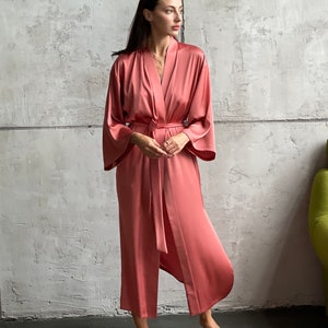 May include: A long, salmon-colored satin robe with a tie belt. The robe has wide sleeves and a relaxed fit.