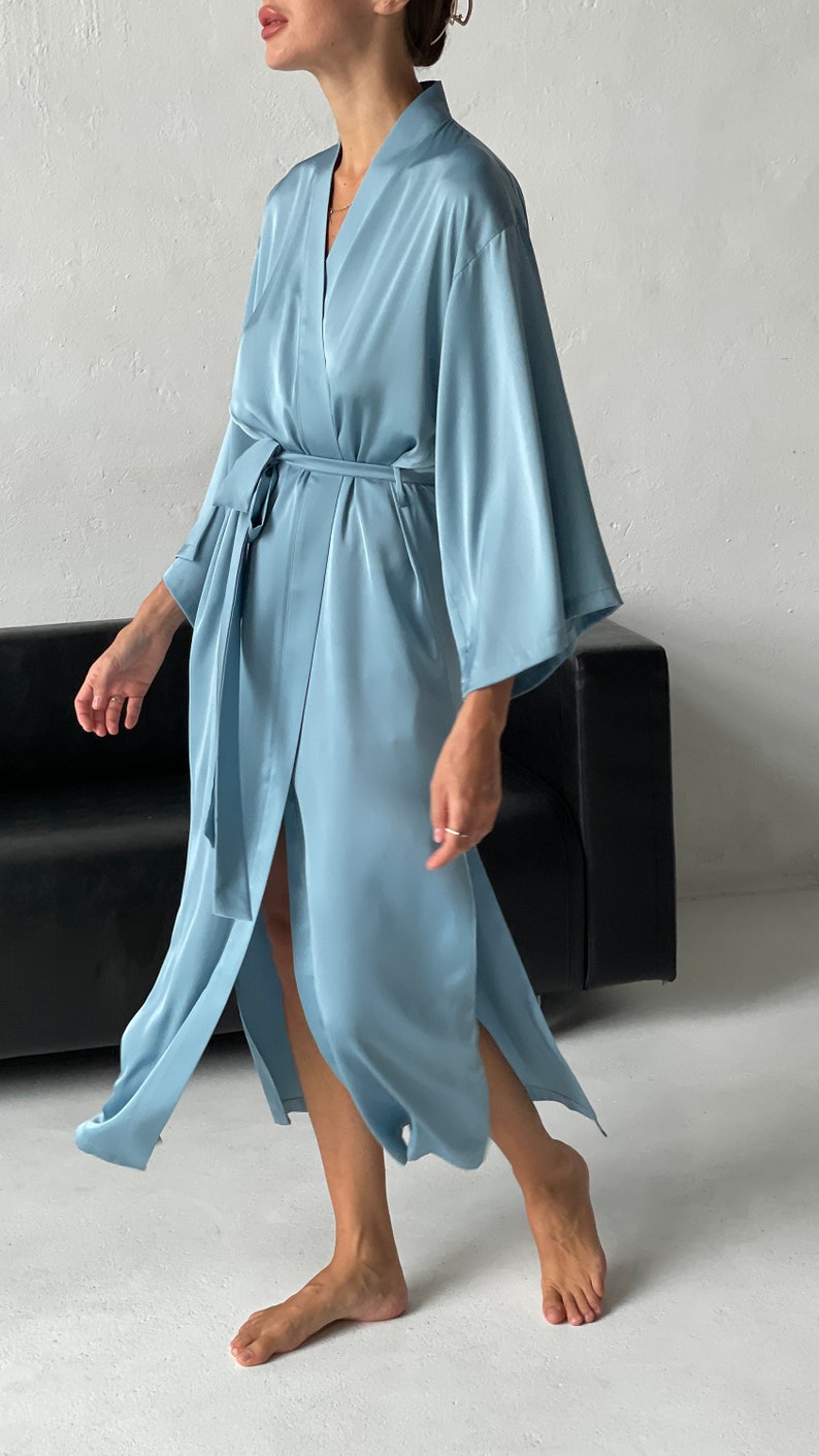 May include: A light blue satin robe with long sleeves and a tie belt. The robe is open in the front, revealing a glimpse of the person's legs.